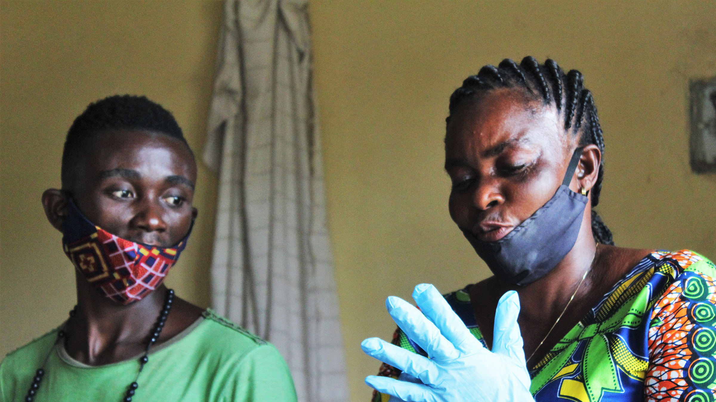 Two people putting on plastic gloves and wearing face masks