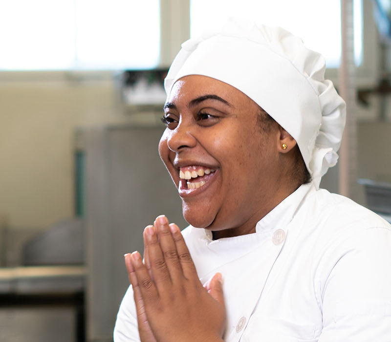 A woman in a chef's uniform laughs