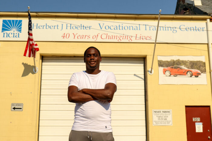 A man stands with arms crossed in front of a garage.
