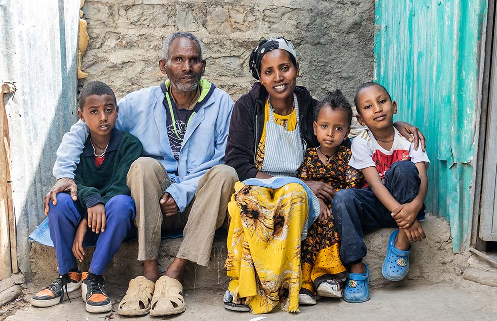 Two parents sit on a step surrounded by their 3 young children.