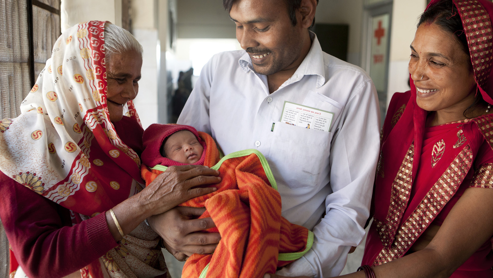 A mother and grandmother looks at a baby being held by a father.
