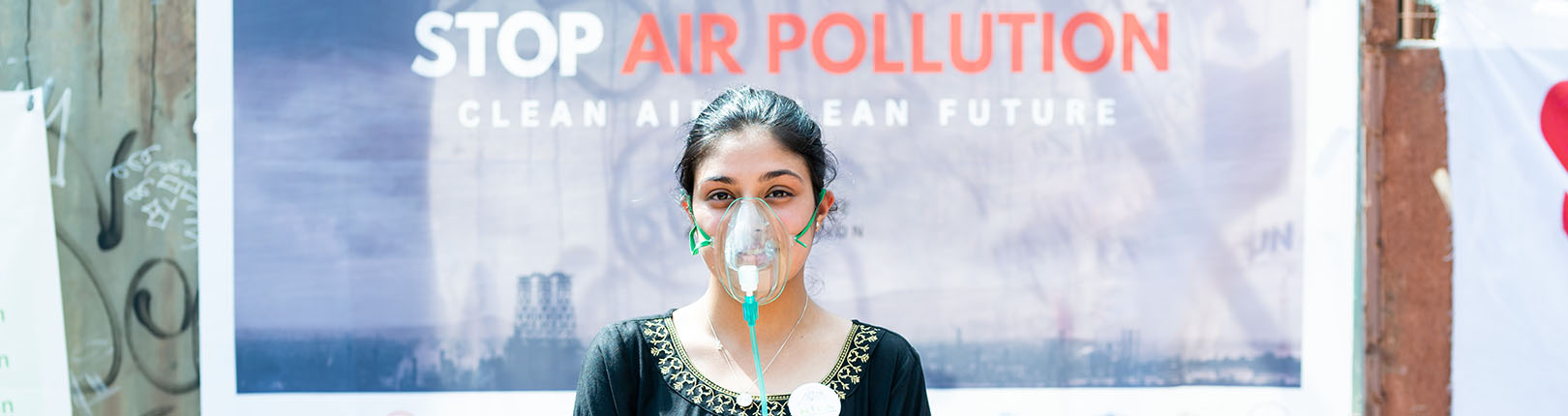 A woman wearing an oxygen masks poses in front of a sign that says "stop air pollution."