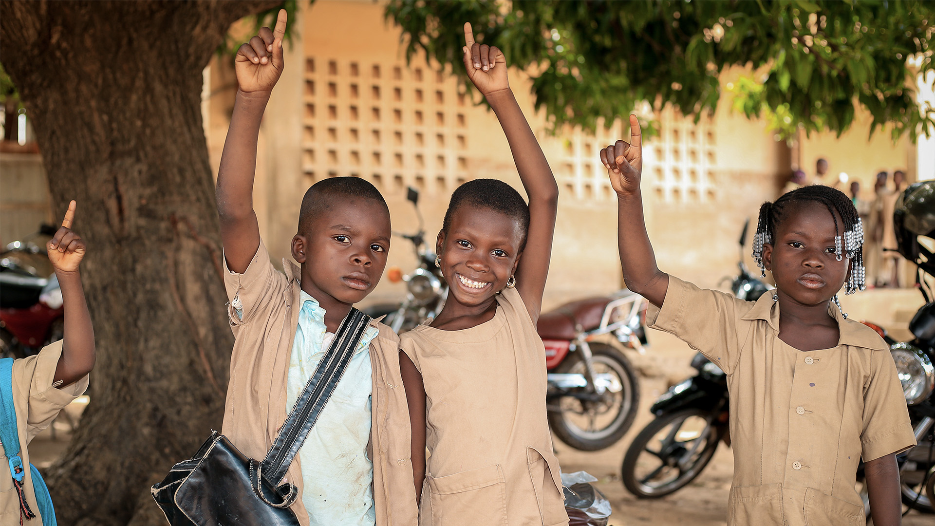 children smiling pointing hands up with pointer finger extended.