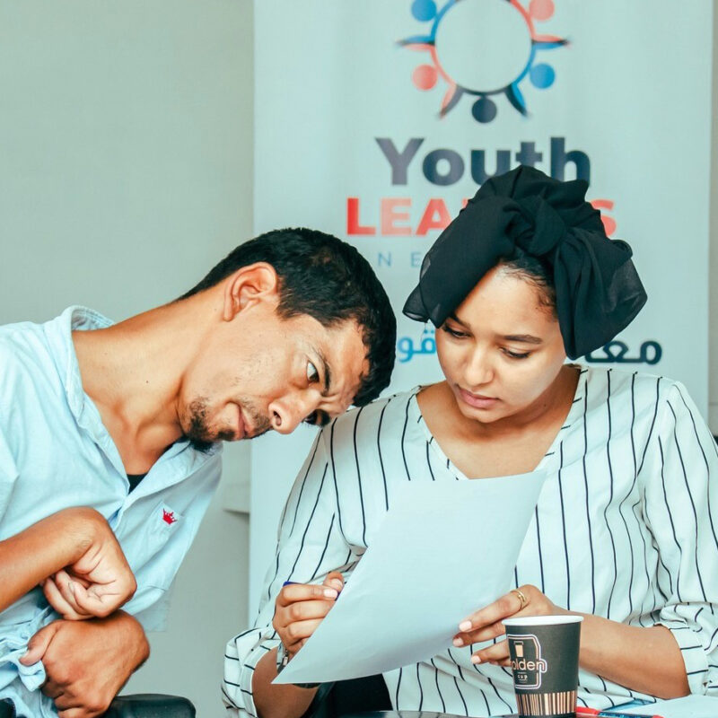 Two people work together, leaning over a paper