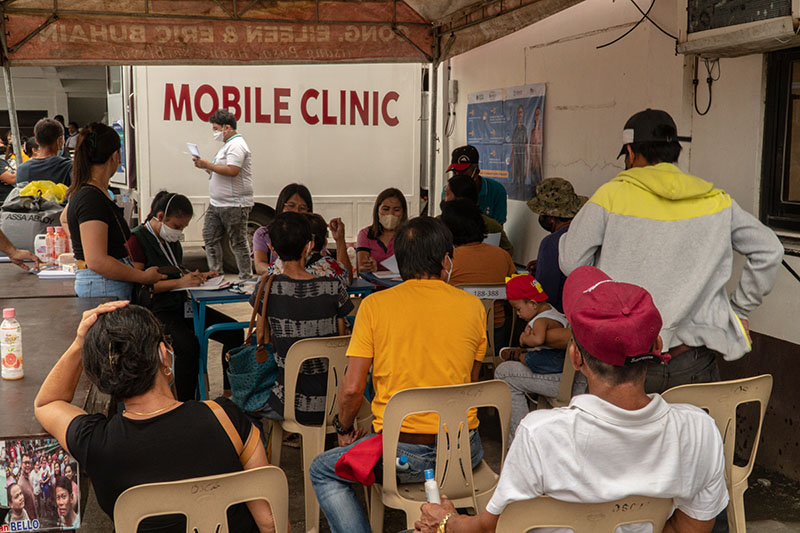 A group of people wait in front of a sign that says "mobile clinic"