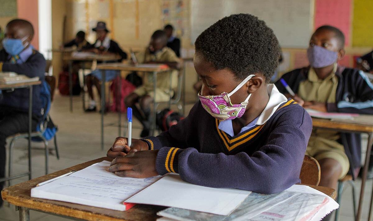 A girl wearing a face mask writing in her notebook at her school desk