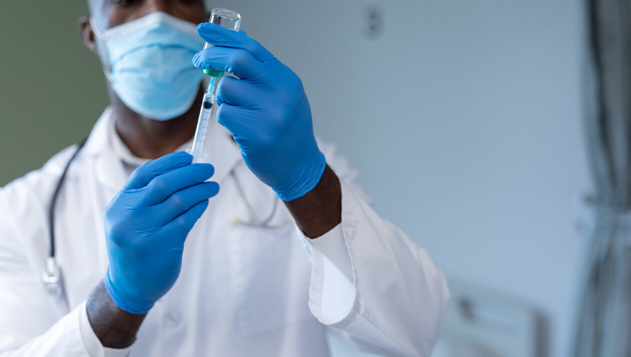 African american male doctor wearing face mask and gloves preparing covid vaccination.