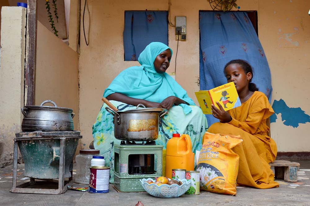 A young girl in Djibouti reads out loud from a picture book while seated next to her mother.