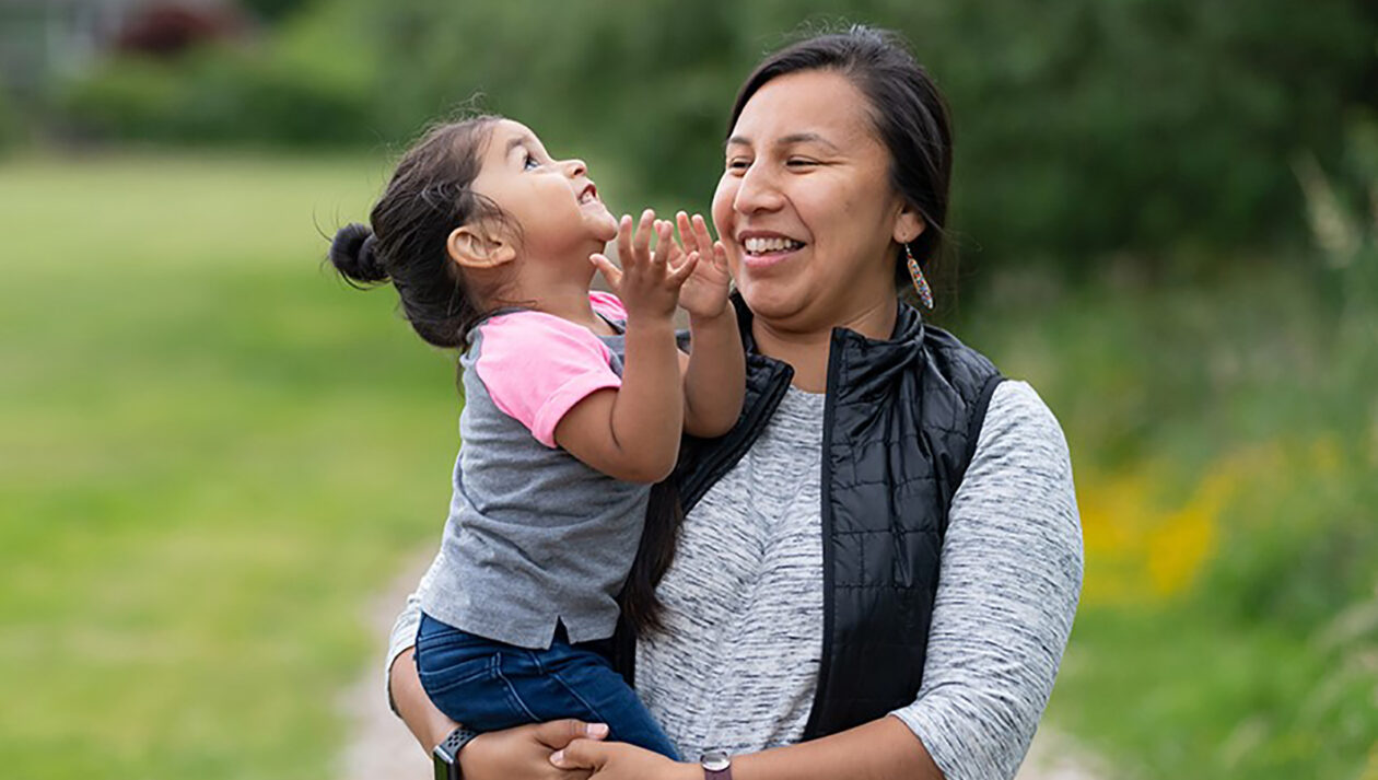A woman holds her young daughter in her arms and laughs