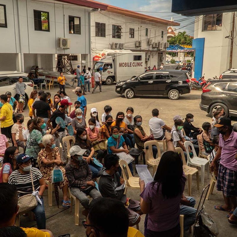 A group of approximately 50 people sits in chairs in an outdoor courtyard in the Philippines.