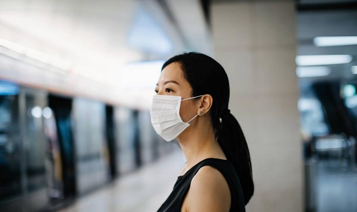 A woman wearing a face mask waits for a train