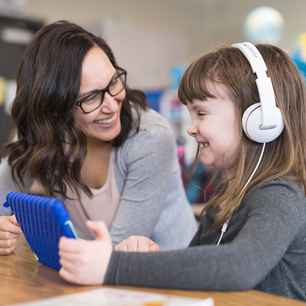 teacher smiling to student using headphones and a tablet