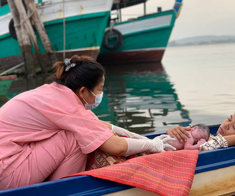 A nurse places a newborn baby on a mother's chest while in a small canoe on the water.