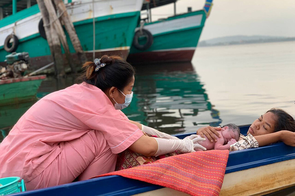 A nurse places a newborn baby on a mother's chest while in a small canoe on the water.