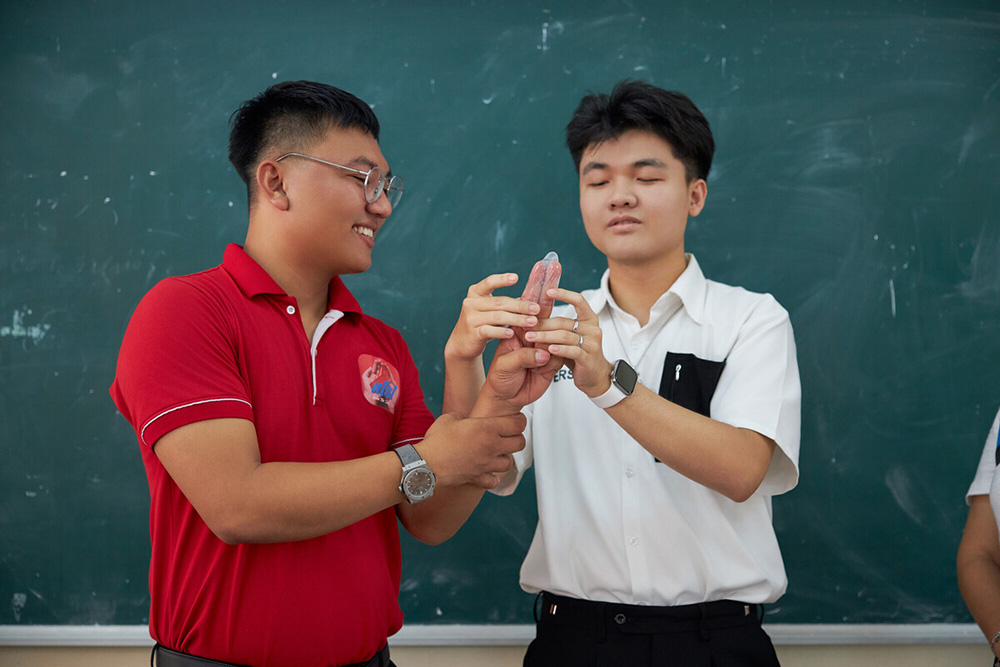 Two young men use their hands to demonstrate how to put on a condom.