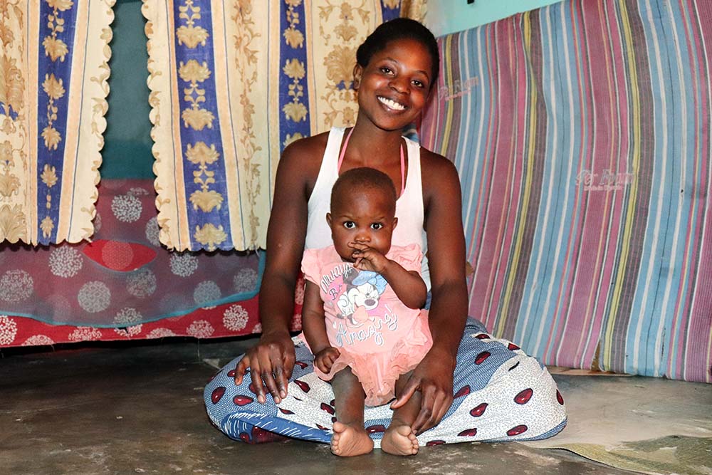 A woman sits smiling on the floor with her baby on her lap.