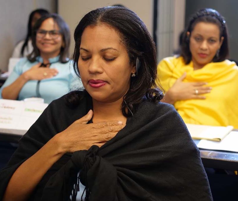 A group of women sit in a classroom with their hands laid on their chests, practicing mindfulness