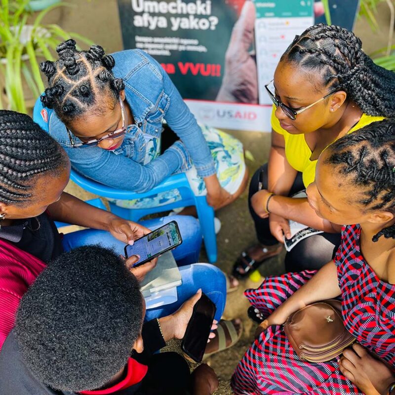 5 young women seated in a circle look at a mobile phone