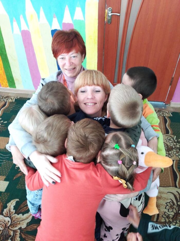 Dariia Bui (center) and Olena Smyrnova share a hug with kindergarten students and Hugging Goose. Photo credit: Oksana Kozlovska
