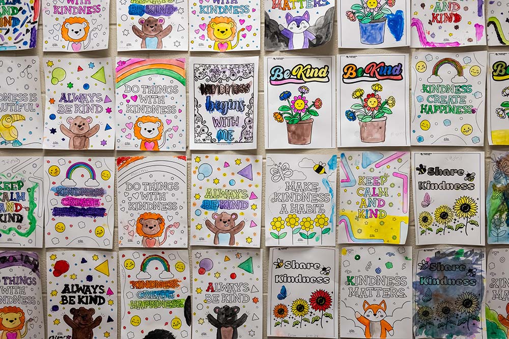 A wall displaying cards that were colored by the kids. The cards say things like "Kindness begins with me" and "Make kindness a habit."