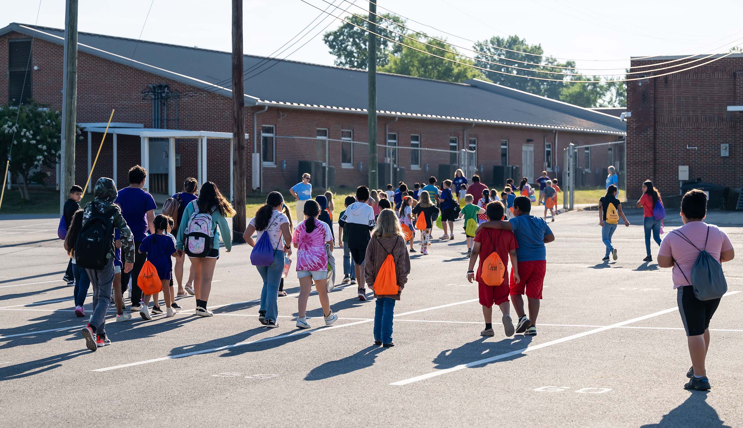 A large group of children pictured from behind as they walk into a school building.