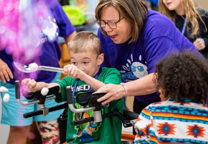 A teacher and a young student have fun playing a game involving trying to catch cotton balls with a plastic spoon.