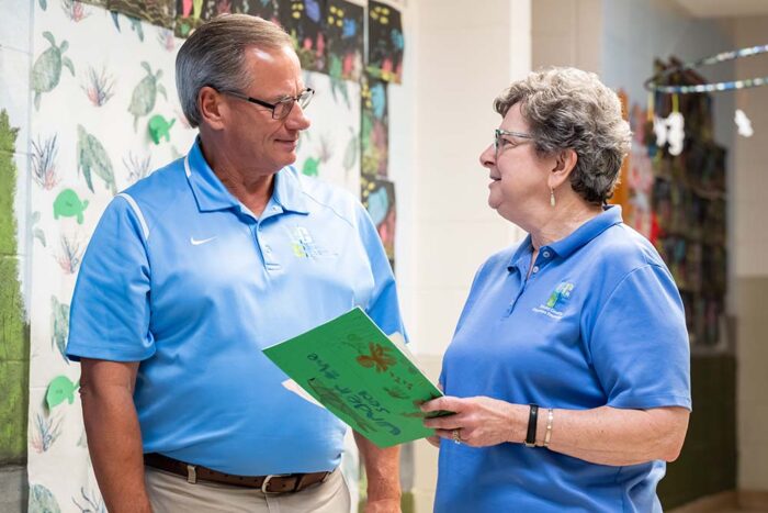 A man and a woman both in light blue polo shirts have a friendly discussion.