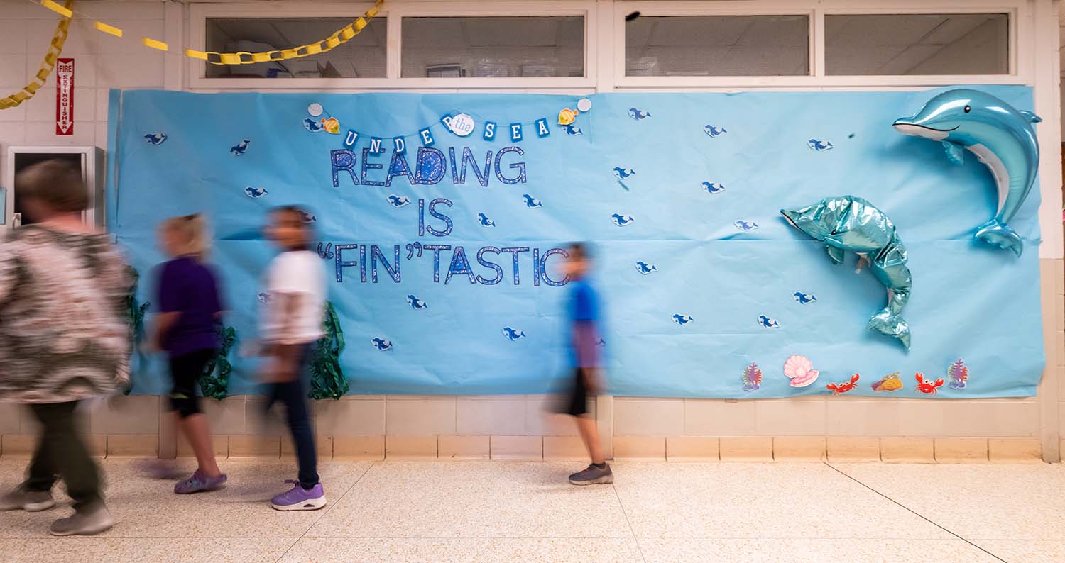 A large blue poster on a wall in the school that says "Reading is 'fin'tastic, surrounded by illustrations of dolphins.