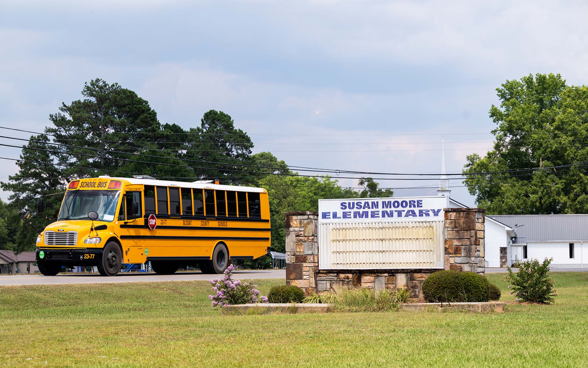 A yellow school bus drives past the entrance sign for Susan Moore Elementary school.