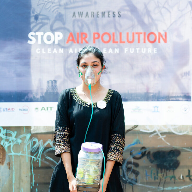 woman with mask on in front of stop air pollution sign