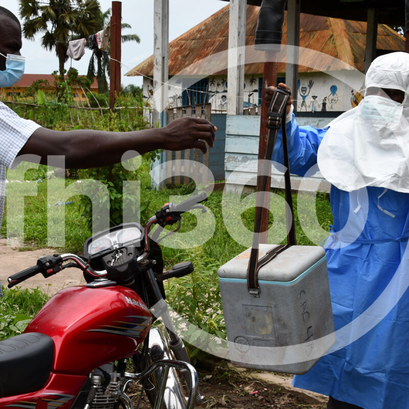 man wearing PPE hands off medical specimen to man who will transport by motorcycle