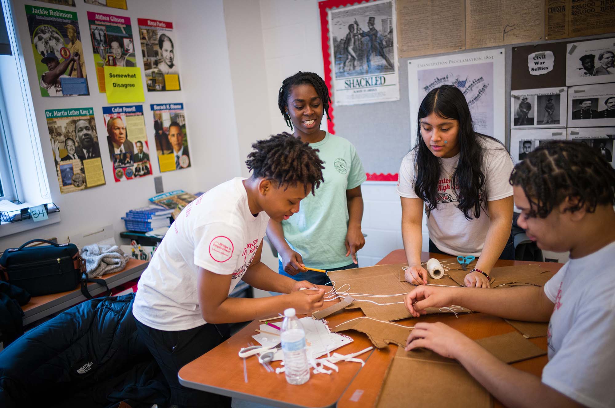 4 students are seen working on a project with cardboard, string and tape.