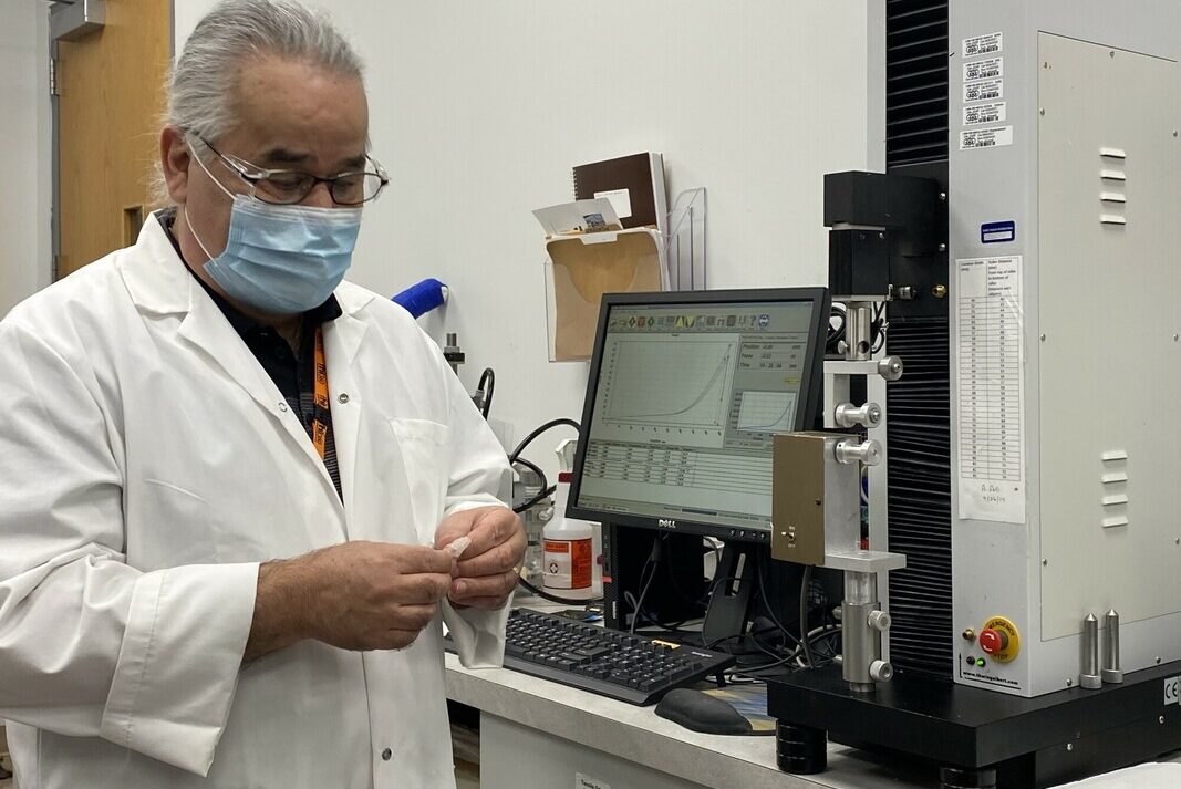 A lab technician stands in front of a computer in a lab, holding a small object.