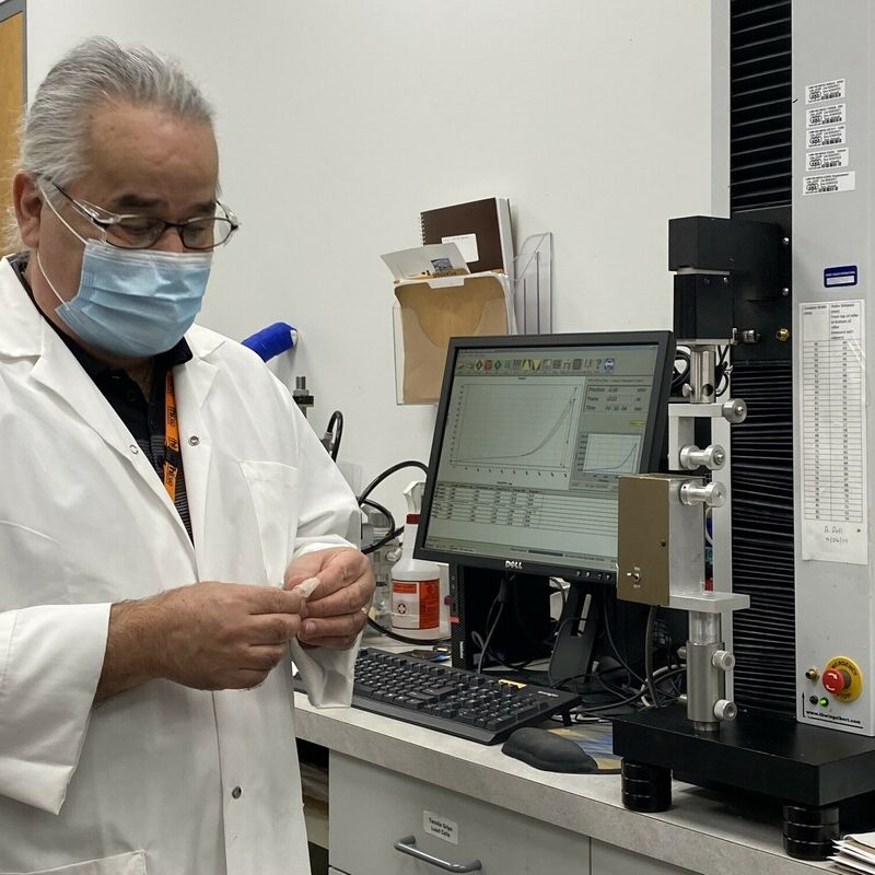 A lab technician stands in front of a computer in a lab, holding a small object.