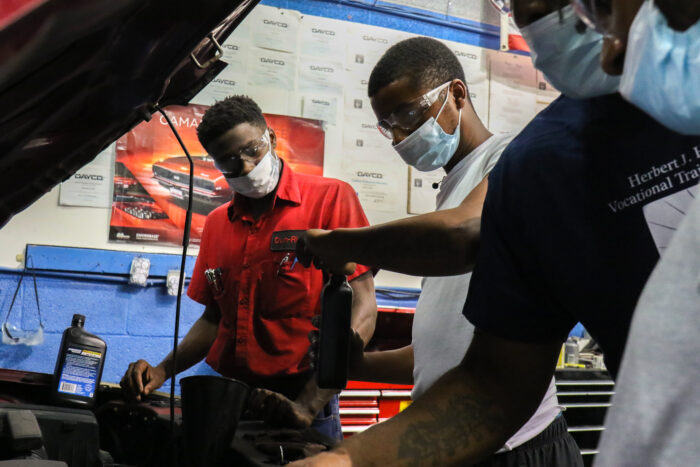 A teenage student opens a bottle of motor fluid while another student looks on.