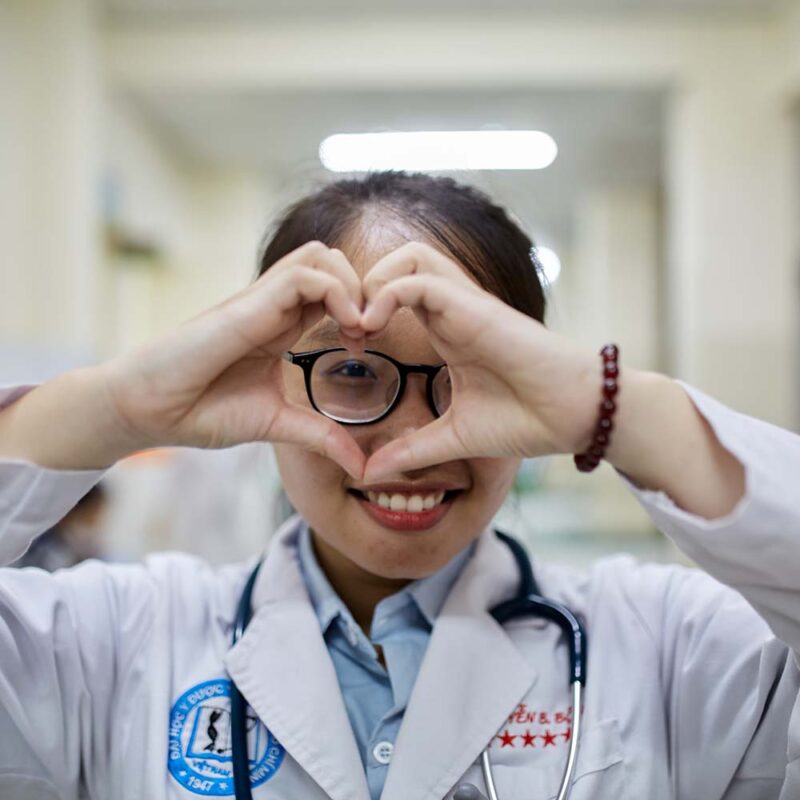A female physician makes a heart symbol with her hands and smiles.