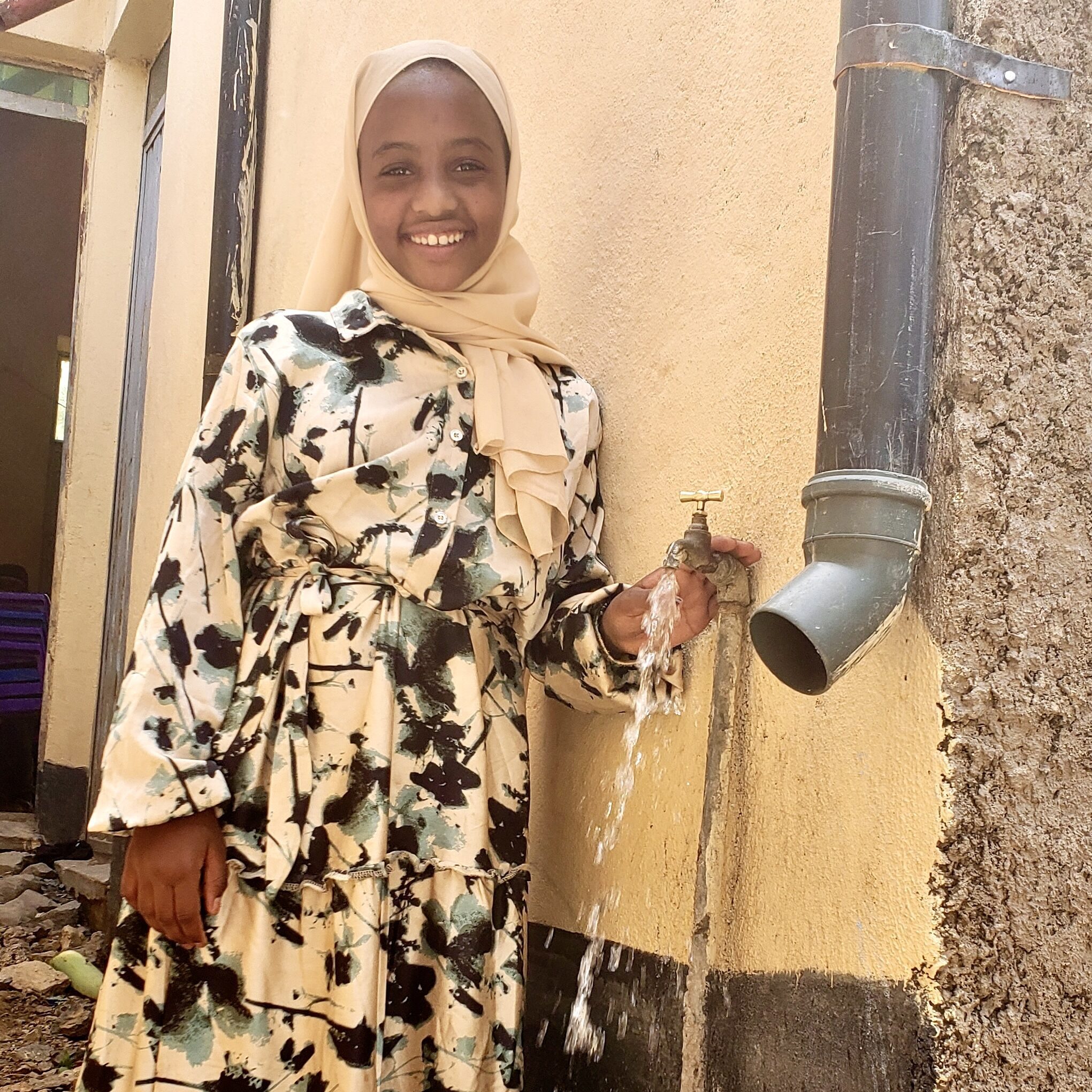Eman stands in front of her community's new functioning water tap