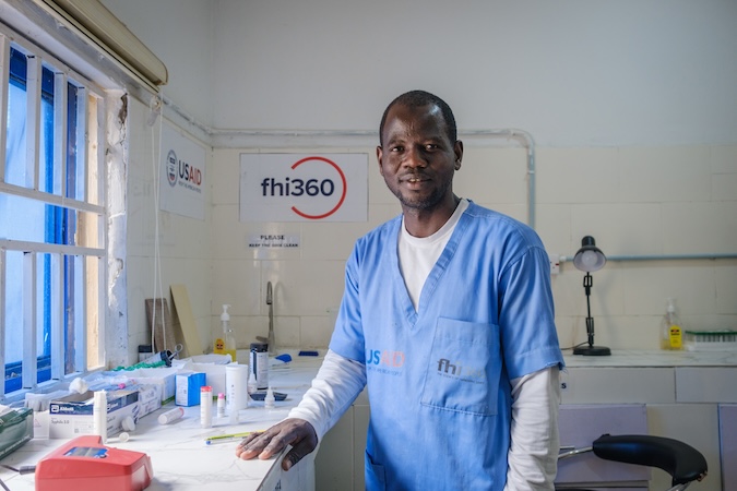 A man in scrubs smiles in a medical setting. 