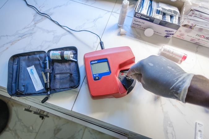 A hand in a medical glove holds a test strip to a red medical machine.
