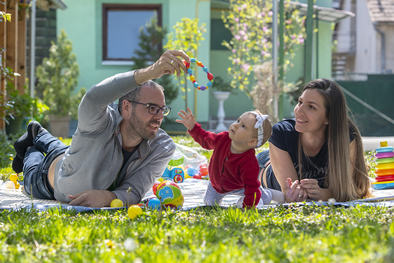 Parents in Serbia play with their child on a blanket outdoors in the sunshine as part of a playful parenting learning experience.