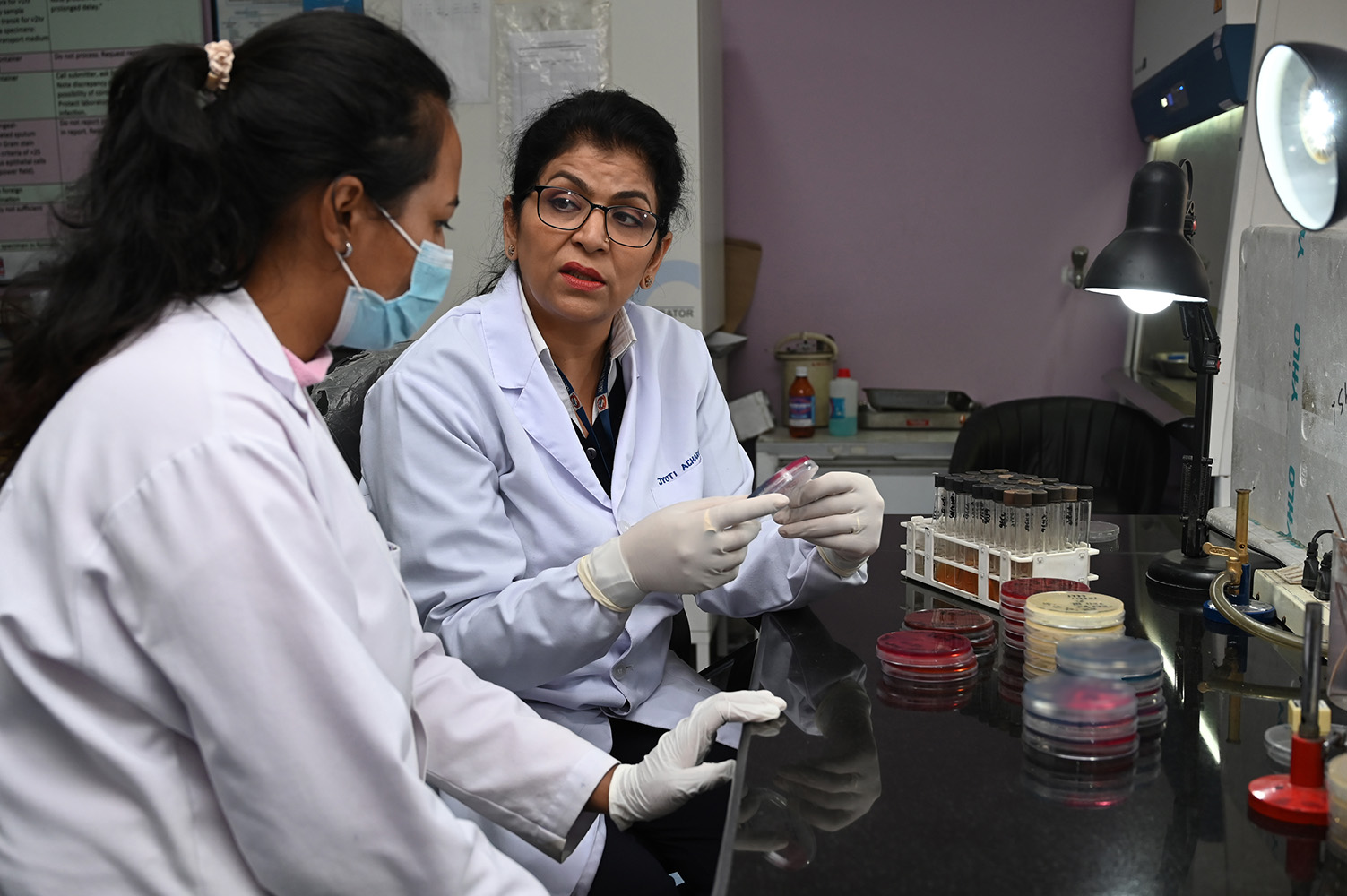 Jyoti Acharya, chief medical laboratory technologist at Nepal’s Bir Hospital, shows microbiologist Sanju Maharjan a bacterial culture technique involving an agar plate.