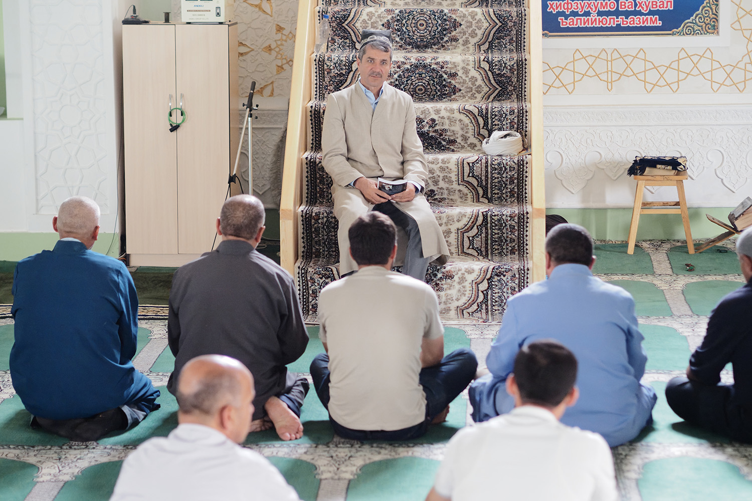 Imam Azalshoh speaks about TB to a group of seated men at Friday prayers.