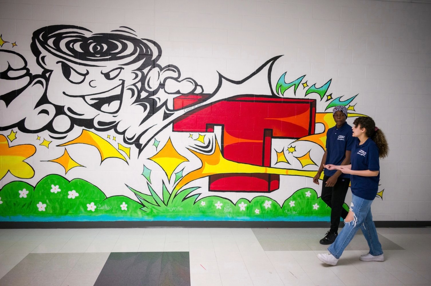 Two students walk down a hallway with artistic graffiti on the wall.