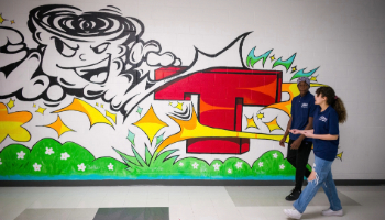 Two students walk down a hallway with artistic graffiti on the wall.
