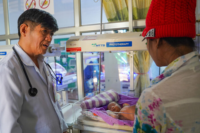 Doctor talking to someone both overlooking a baby in an incubator.