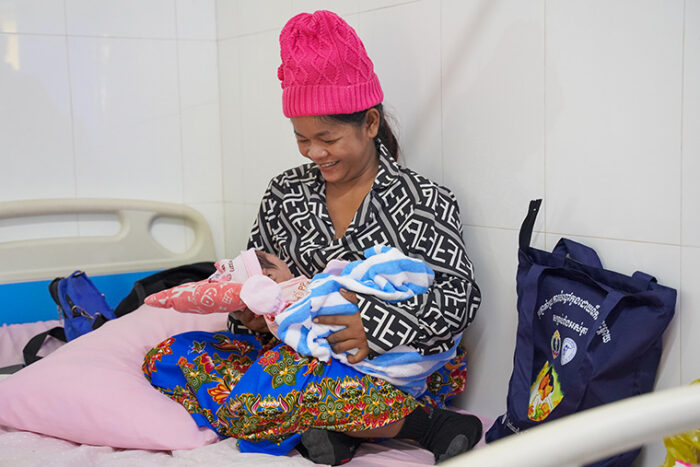 A smiling woman sits in a hospital bed holding her baby.