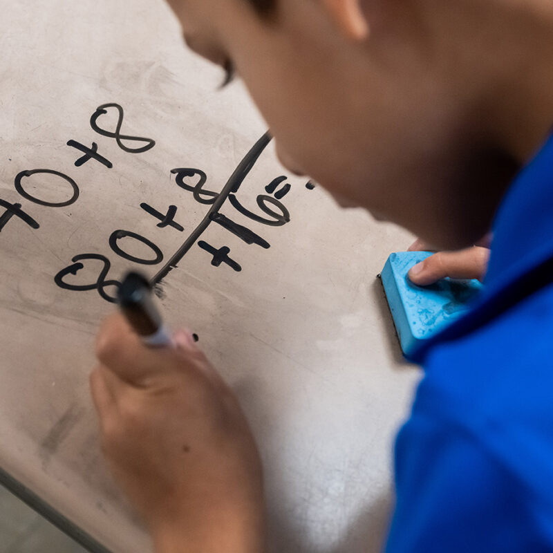 A boy uses a marker on a dry erase board to write math equations.