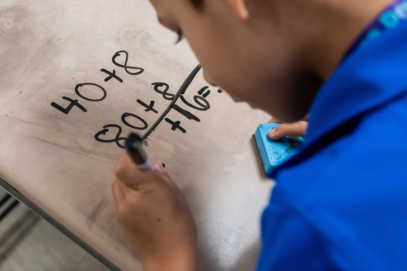 A boy uses a marker on a dry erase board to write math equations.