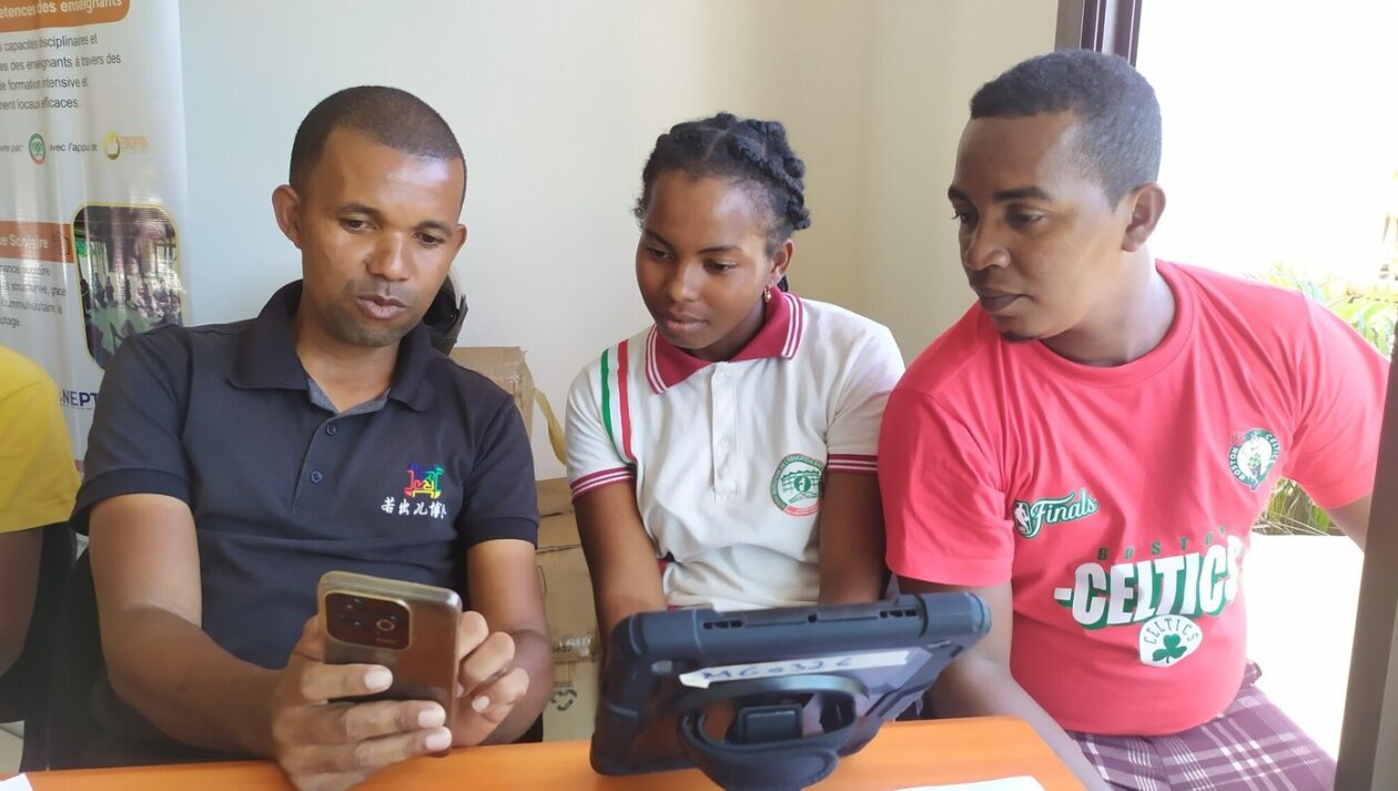 A man shows something on his phone screen to a young woman and young man.