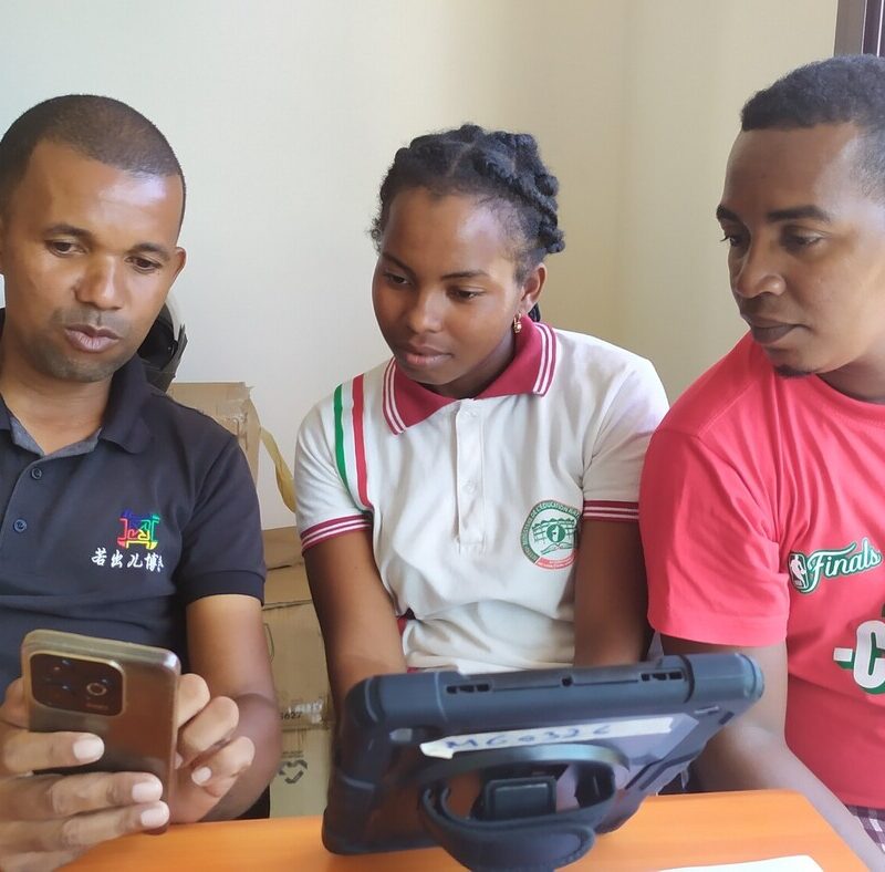 A man shows something on his phone screen to a young woman and young man.